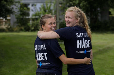 To piger der holder om hinanden og smiler til kameraet